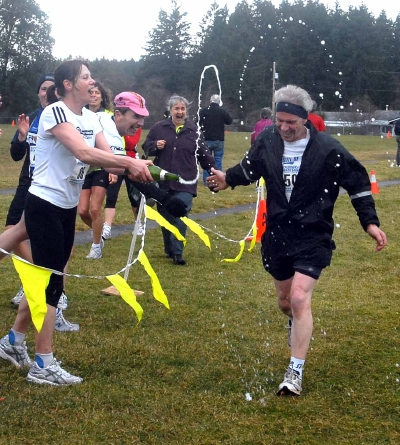 Under a shower of champagne from the women who helped save his life after a heart attack a year ago, Ken Pungente crosses the finish line of the Cedar 12K.. Photograph by : GLENN OLSEN, NANAIMO DAILY NEWS